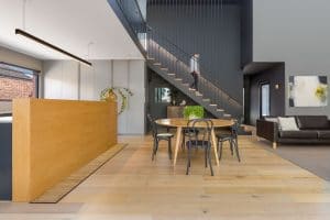 house contemporary Living area architectural photograph showing hydronic heating trench product in front of quality timber finish kitchen island with timber grate matching timber flooring with view of lady walking down stairs in background dining table and couch seating