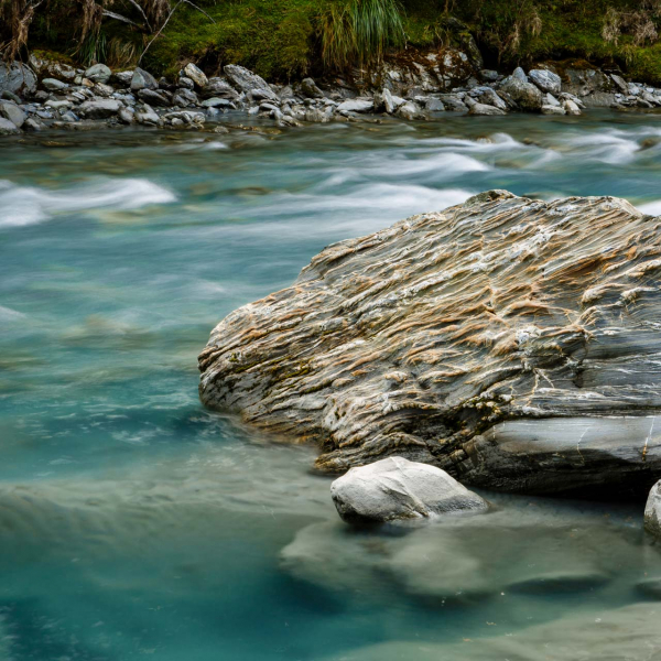 queenstown landscape river wth large rock photographed with slow shutter speed to blur water flowing in river